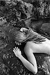 Young nude Asian woman lying face down on rocks.