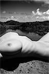 Close up torso of young adult nude Caucasian woman lying on boulder on rocky Maui coast.