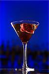 Still life of martini cocktail with raspberry fruit against glowing blue background.