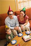 Caucasian boy and parents in party hats eating birthday cake.