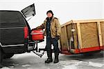 Caucasian man unloading cooler from truck with trailer on frozen lake going ice fishing in Green Lake, Minnesota, USA.