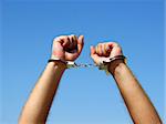 The hands of the men chained in handcuffs, on a background of the blue sky