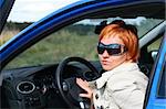 Red-haired young woman in sun glasses in a blue car