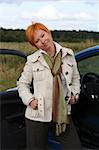 Young woman is standing near blue car in a field