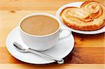 Closeup of coffee with milk in white cup and a palmier pastry. Shot on light wood background