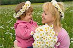 Baby girl picking flowers with her mother in a field full of daisies