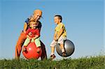 Woman and kids jumping on large balls in the grass under clear blue sky