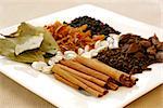 An assortment of fragrant, richly flavored spices - bay leaves, mace, peppercorns, black pepper, silver cardamom pods, cloves and cinnamon. Focus on the cinnamon sticks.