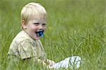 A 2 year old sitting in the grass.