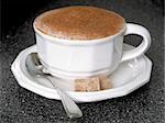Hot cappucino with spoon and sugar cubes.