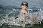 young boy with goggles playing in the water, splashing