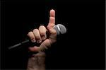 Microphone clinched firmly in male fist with index finger pointing up.
