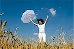 Happy young girl jumping for joy with umbrella in the field