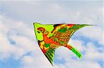 A kite flying against a blue sky in sunlight, bright colors and streaming tail