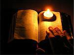 On a photo a candle which on the Bible. A photo on a dark background of a table. The photo is made in Ukraine.