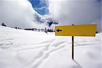 Mountain panorama during sunny day in Alps with yellow sign showing which way shoul You go