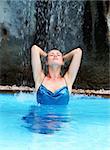 Lovely woman under a waterfall in a pool.