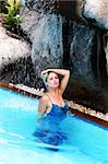 Young blond woman under a waterfall in the pool with an evening gown on - trash the dress trend.