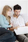 A young woman suggestively approaches her man who is working on his laptop