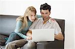 A young couple at home on the sofa looking intensely at their laptop