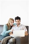 A young couple at home on the sofa excited about what they're seeing on their laptop computer