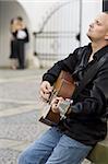 A street musician playing his guitar serenades a romantic couple kissing out of focus in the background