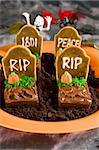 Halloween tombstone made of  brownies and sugar cookies on a bed of crashed oreo cookies