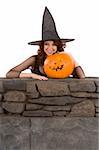 Portrait of Hispanic teenager girl in black Halloween hat and fishnet dress with carved pumpkin (Jack O' Lantern)