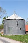 Metal grain silo for storing animal feed set against a blue sky.