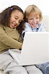Two young children having fun on a laptop computer while sitting on a settee