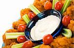 Closeup view of spicy buffalo chicken wings with ranch dressing, celery and grape tomatoes.