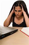 Young Hispanic woman sitting in front of desk looking at laptop computer with hands on head looking tired or frustrated