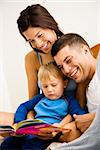 Caucasian parents and toddler son reading book.