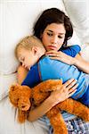 Caucasian mid adult woman holding sleeping toddler in bed.