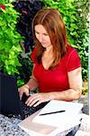 Mature woman working on portable computer in her garden at home