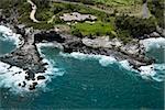 Aerial view of rocky coastline on Maui, Hawaii with rooftop view of building and road.