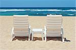 Two sun beach chairs on beach sand near ocean