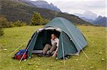 Mountaineer in his tent on a meadow with mountains in the background