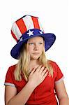 A pretty American girl in a stars and stripes hat, solemnly saying the pledge of allegiance.  Isolated on white.