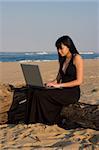 Attractive woman working on a laptop with the beach as background