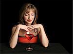 A beautiful woman in red, drinking a cosmopolitan with a suggestive expression.  Photographed against a black background.