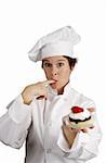 A pretty chef holding a strawberry cheesecake tart and licking whipped cream from her finger.