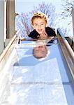 Young boy laying on top of slide at outdoor playground