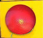 Extra large red light is framed by the yellow metalic frame of a traffic light.  Light is glowing red.