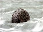 A rock poking out of the water with waves crashing all around. Long shutter speed.