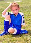 Sweaty young boy sitting on grassy soccer field resting at halftime