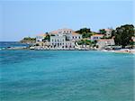 A part of Spetses island town, Greece; traditional houses, a small beach, and a lighthouse can be seen