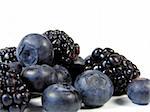 closeup of blueberries and blackberries isolated on white in a pile with focus on the left on the top blueberry