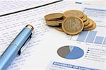 Business background: Financial reports, euro coins and a blue pen (focus on the coins)