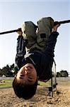 Young asian boy hanging upside down on a playground structure